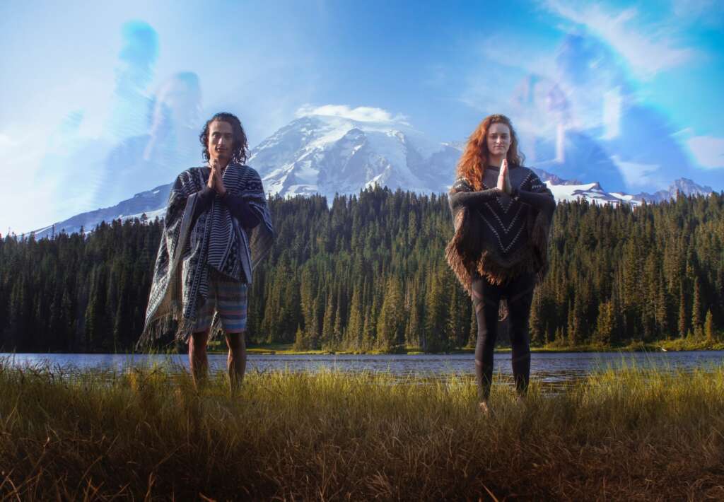Two people standing in a field by a lake with rainbow editing in the sky
